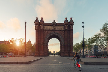 Tourist riding bicycle near Bacelona Arc de Triomf during sunrise in the city of Barcelona in Catalonia, Spain. - obrazy, fototapety, plakaty