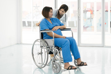 Fototapeta na wymiar Asian woman Doctor talking to young pregnant woman in wheelchair at hospital. Beautiful asian doctor taking care of patient in wheelchair..