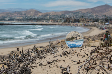 Sunny summer day on the Ventura beaches with puffy clouds visible in blue sky through round sphere lens on sand.