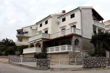 Mediterranean style white and traditional stone building with multiple apartments on street corner surrounded with other buildings and vegetation closed for winter