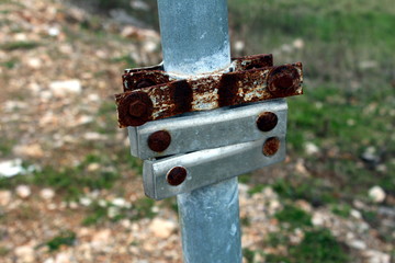 Rusted and new metal round post mount brackets for holding signs mounted on grey metal post with...