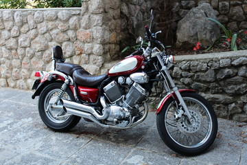 Fototapeta na wymiar Modern new and polished red and chrome chopper parked in front of stone wall with flowers planted in the middle