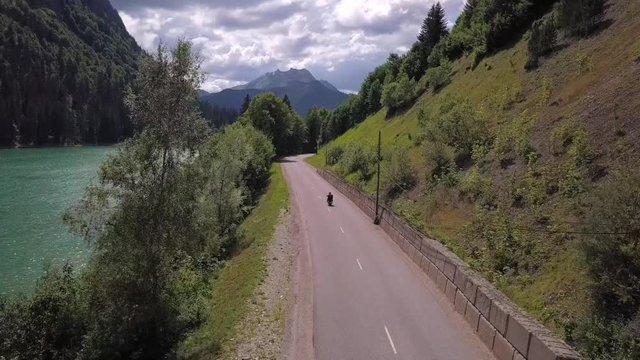 Aerial view of a motorcycle next to a lake, with a view of a mountain in the background. It's in the north alps, near Morzine.