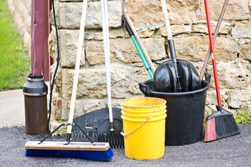 Cleaning tools leaning against the wall. Equipment for outdoor cleaning.Brooms, rakes, plastic yellow and black buckets, black plastic shovel.