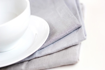 Empty white plate and bowl on a stack of gray napkins on a table.