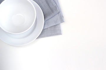 Empty white plate and bowl on a stack of gray napkins on a table.