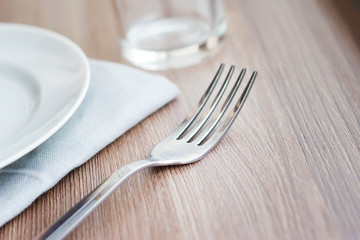 Empty white plate on a gray napkin with fork and glass on brown table. Table setting, preparation for meals.
