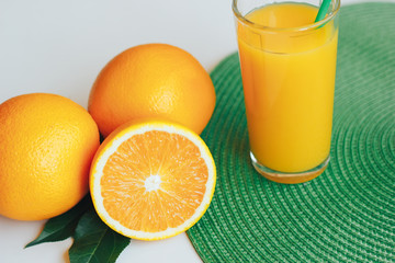 Glass with orange juice next to orange slices on a white and green background.