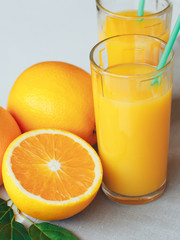 Glass with orange juice next to orange slices on a gray background.