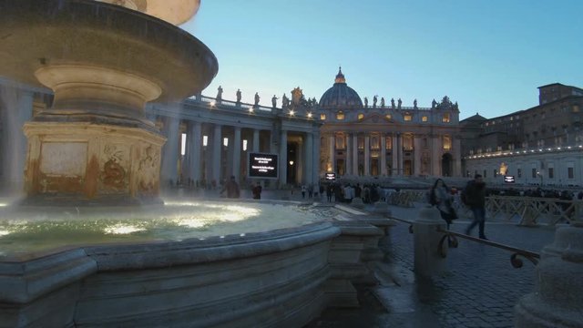 4K Timelapse - Rome, Vatican, Saint Peter square. 
It is dusk time and a large baroque ancient fountain in foreground. Many tourists walk and take photos and selfies
