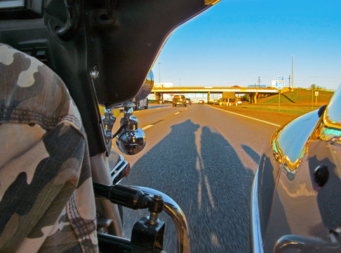 Three-wheel Motorcycle Riding On The Texas Highway At Sunset. Evening Landscape With Long Shadow Of Motorbike On Asphalt, Road Signs And Bridge.  