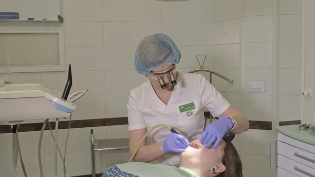 Woman at dentist clinic gets dental treatment to fill a cavity in a tooth. Dental restoration and composite material polymerization with UV light and laser. The doctor works with an assistant.