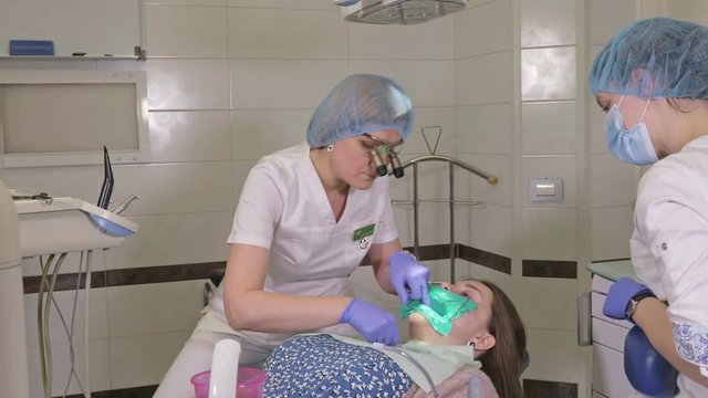 Woman at dentist clinic gets dental treatment to fill a cavity in a tooth. Dental restoration and composite material polymerization with UV light and laser. Installation of dental dam.