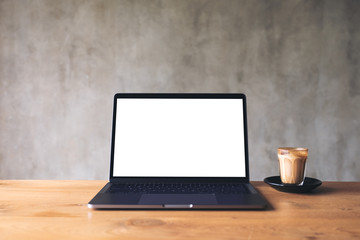 Mockup image of laptop with blank white desktop screen and coffee cup on wooden table with brick wall background