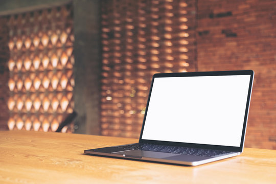 Mockup image of laptop with blank white desktop screen on wooden table with concrete wall background