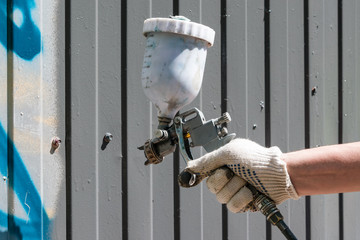 Man's hand in glove spray painting metal fence, close-up