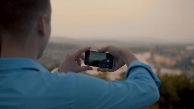 Man Gets Phone from His Pocket and Takes a picture in sunset. Smartphone Photography of City