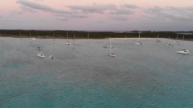 Harbor full of sailboats off island coast in the Exumas, Bahamas. Aerial drone view by Mavic Air as pink sunset begins to form over ocean horizon.