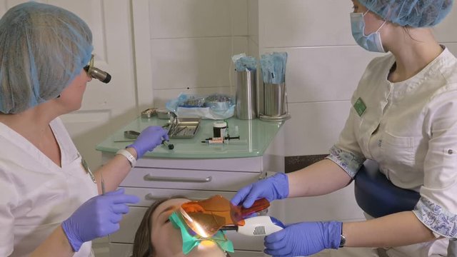 Woman at dentist clinic gets dental treatment to fill a cavity in a tooth. Dental restoration and composite material polymerization with UV light and laser. The doctor works with an assistant.