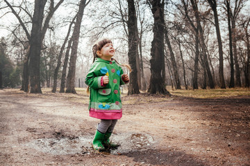 the girl is poking on puddles in rubber boots