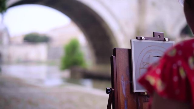 Close-up of artist woman's hand with brush. The process of drawing on canvas: unknown artist paints a fine brush on a canvas. The artist at work draws a picture outdoors