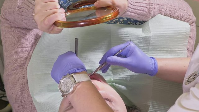 Woman at dentist clinic gets dental treatment to fill a cavity in a tooth. Dental restoration and composite material polymerization with UV light and laser. The patient looks in the mirror.