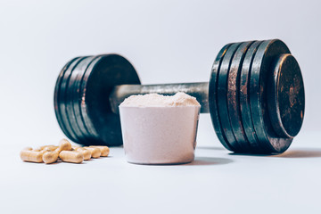 Whey protein powder in a scoop next to heap of vitamin pills