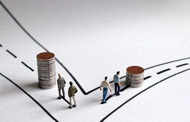 A concept of economic inequality. Two pile of coins and miniature people on two paths.