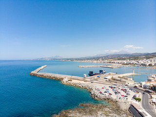 Harbour with marine vessels, boats. View from drone on Bay with beach and architecture Bali - vacation destination resort, with clear turquoise ocean waters, Rethymno, Crete, Greece. June, 2018