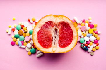  A fresh grapefruit and colorful pills on a pink background. Concept medicine for women's health