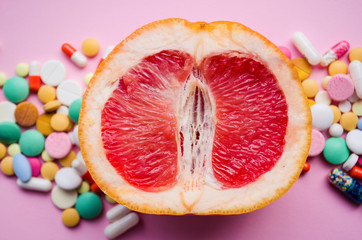  A fresh grapefruit and colorful pills on a pink background. Concept medicine for women's health