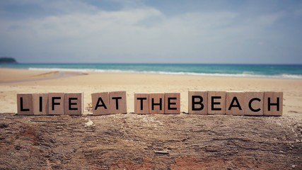 Motivational and inspirational quote - ‘Life at the beach’ written on wooden blocks. Blurred...