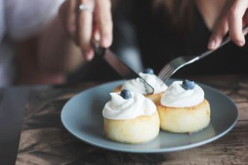 Cheesecakes with cream and blueberries on blue plate, women's hands with knife and fork