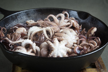 Mini octopus in the process of roasting on a cast iron pan