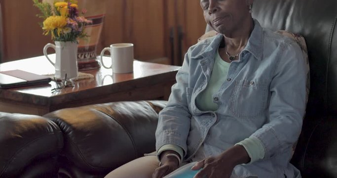 Tilt up of an elderly black woman using an ice pack on her knee to relieve pain