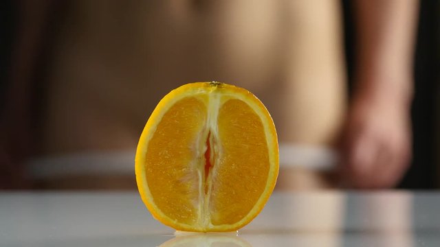 close-up half orange, woman takes off her panties on a dark background. imitation vagina. 4K