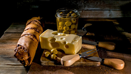 Cheese, olives and appetizing baguette on a wooden background. Low key lighting.