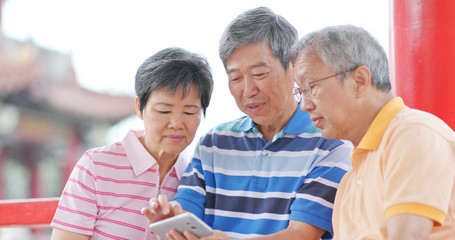 Senior friends talk together look at mobile phone at outdoor park