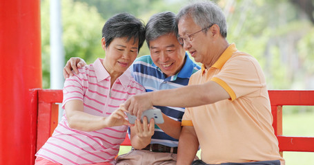 Senior old friends using mobile phone at outdoor park