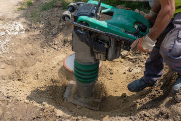 A worker with a vibrating machine compresses the sand