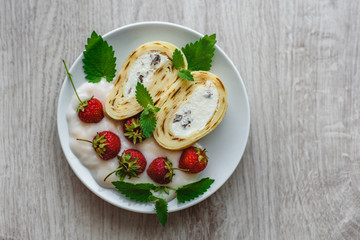 Sweet home pancakes with cottage cheese and strawberries and mint in a white plate on a wooden background