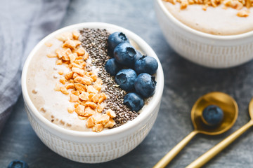 Banana dessert with chia seeds, fresh blueberry and nuts over grey table.