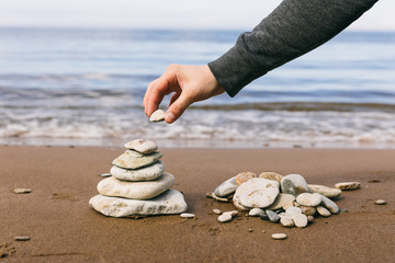 The stone in man's hand on the top of pyramid of stones for meditation on the sea coast. Time management, slow life, simplify
