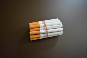 Cigarettes from the pack are fixed with a red rubber band on a brown matte background
