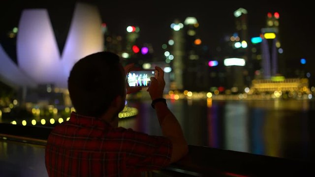 A man is taking pictures of a night city on a smartphone