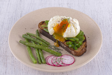 Poached egg on a piece of bread with fried green beans, radish and arugula on a plate