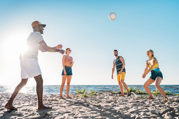happy young multiethnic friends playing volleyball on sandy beach