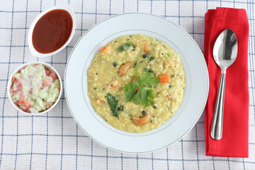 Oats pongal, an healthy, Indian vegetarian food, with raita and tomato ketchup as side dishes, in a ceramic plate.