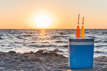 glass bottles with summer drinks and straws on cooler at sandy beach