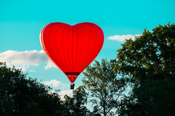 Bright red hot air balloon in the shape of heart against blue sk © smspsy